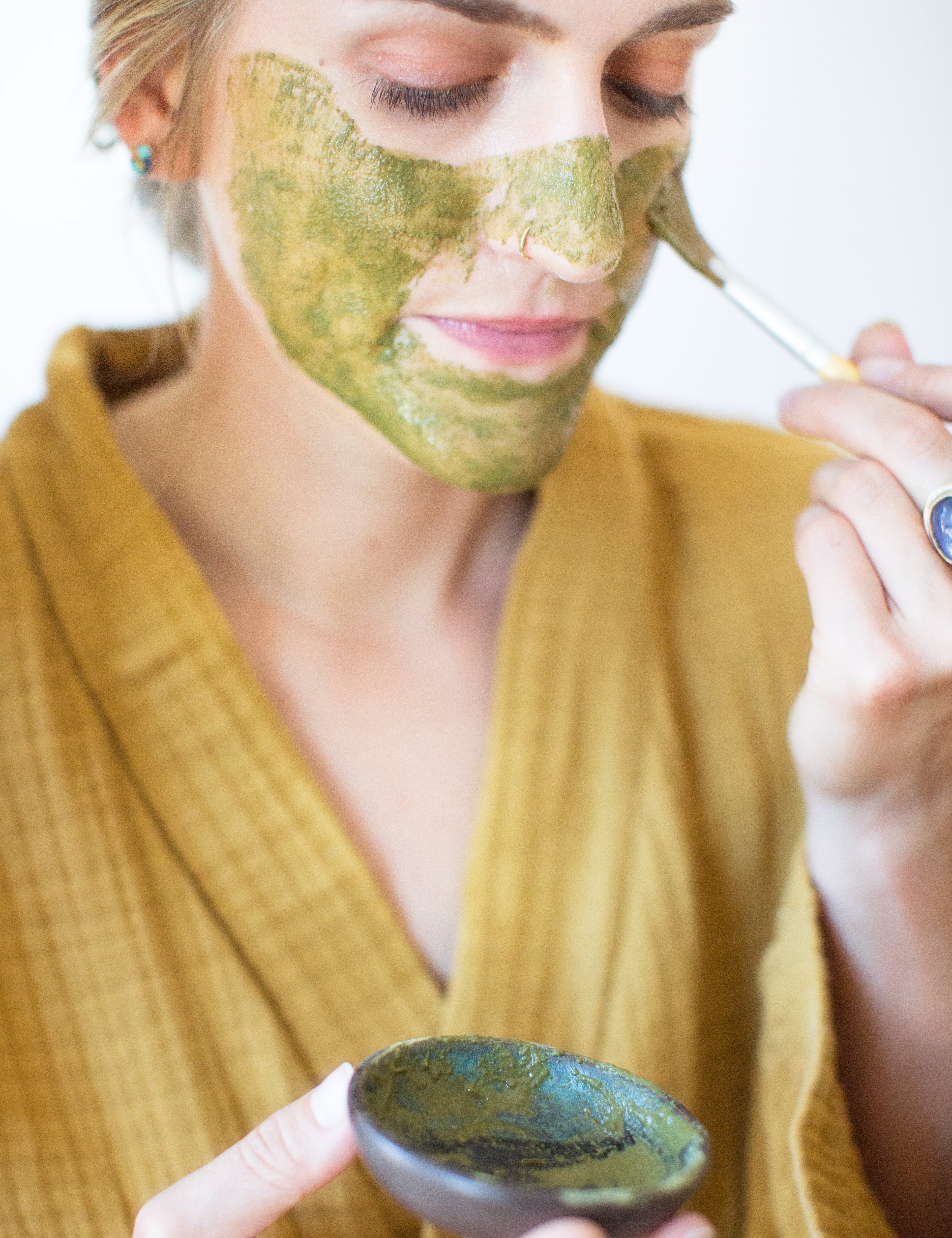 Woman applying face mask to face with brush: Organic herb and clay matcha lavender face mask by Good Flower Farm
