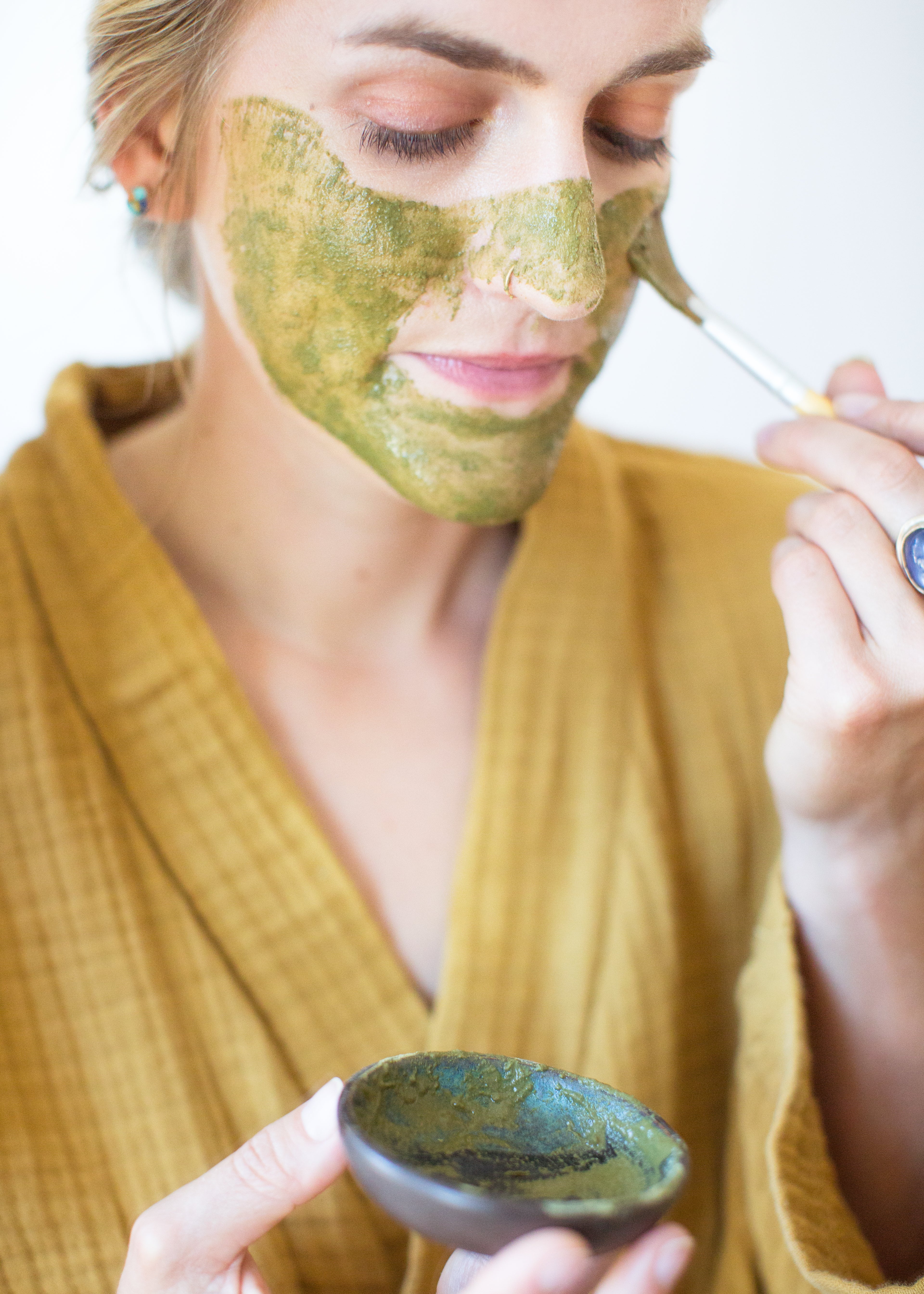 Woman applying face mask to face with brush: Organic herb and clay matcha lavender face mask by Good Flower Farm