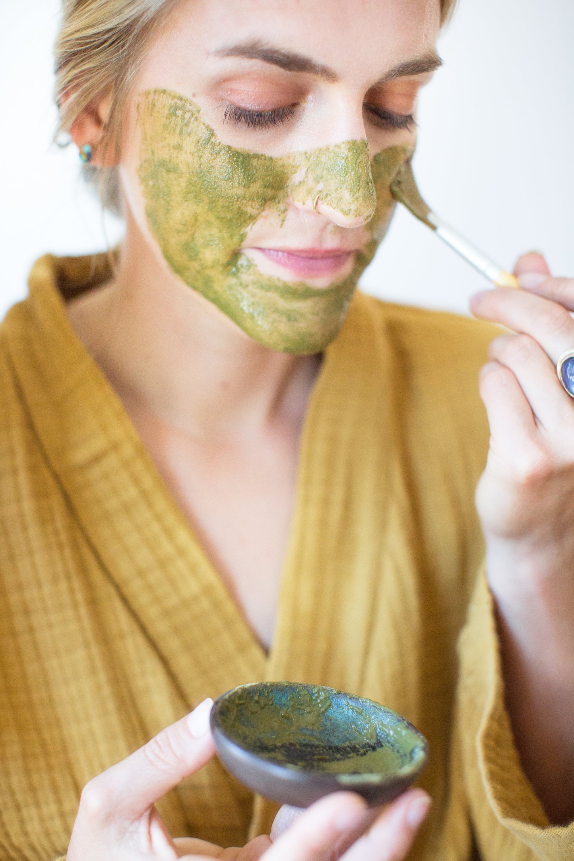 Woman applying face mask to face with brush: Organic herb and clay matcha lavender face mask by Good Flower Farm
