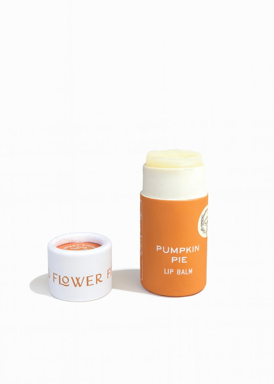 A tube of Good Flower Farm’s SEASONAL LIMITED Pumpkin Pie Organic Lip Balm, cap off and beside it. The orange and white tube contains pale yellow balm made with coconut oil for soft, smooth lips.