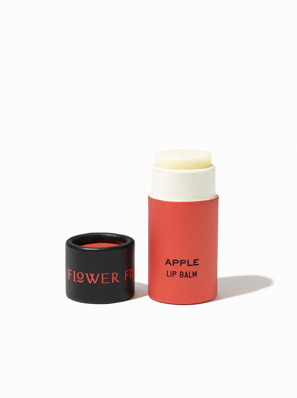 A red tube of SEASONAL LIMITED Apple Organic Lip Balm by Good Flower Farm with the cap off, revealing the balm inside. The black cap has FLOWER in red, and APPLE LIP BALM is printed on the tube. Background is white.