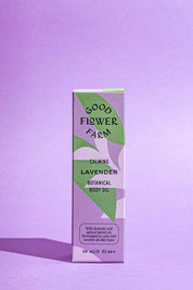 A rectangular box of Good Flower Farm Lavender Botanical Body Oil stands upright on a purple surface with a matching background. The elegant purple and green packaging highlights this soothing body oil with hemp seed oil.