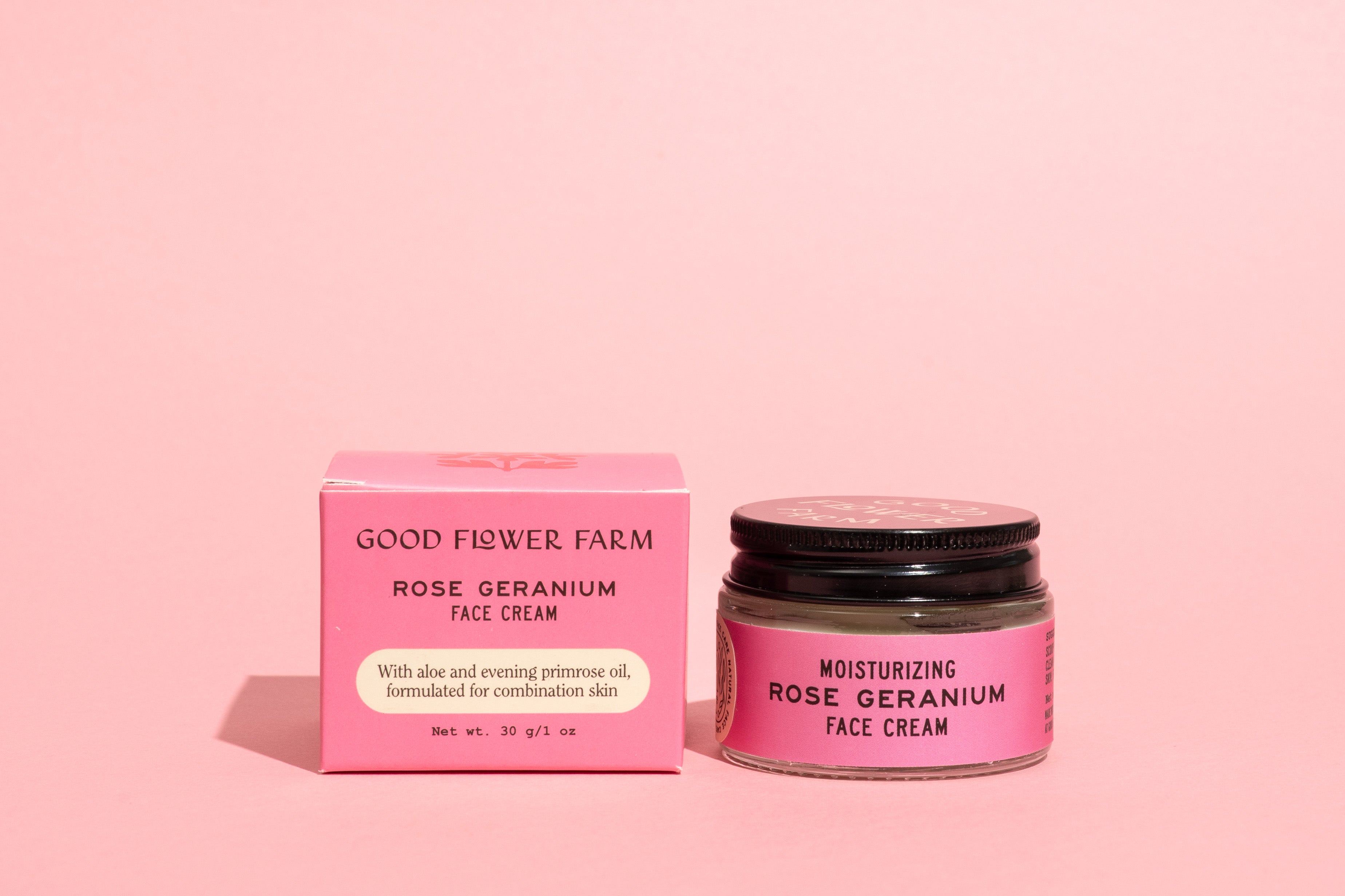 A jar and box of Good Flower Farm Rose Geranium Face Cream are shown on a pink background. The pink containers with black text highlight this moisturizing cream for combination skin, featuring aloe vera and evening primrose oil.