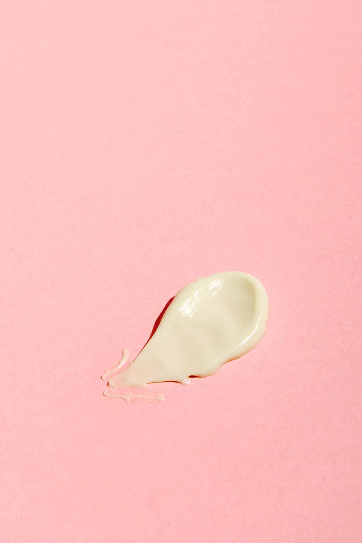 A dollop of Good Flower Farms Rose Geranium Face Cream is spread on a smooth, pastel pink background.