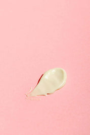 A dollop of Good Flower Farms Rose Geranium Face Cream is spread on a smooth, pastel pink background.