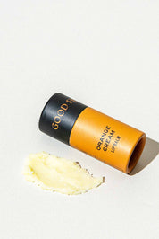 An open tube of Good Flower Farm Orange Cream Organic Lip Balm rests on a light surface beside a small smear of the moisturizing balm.