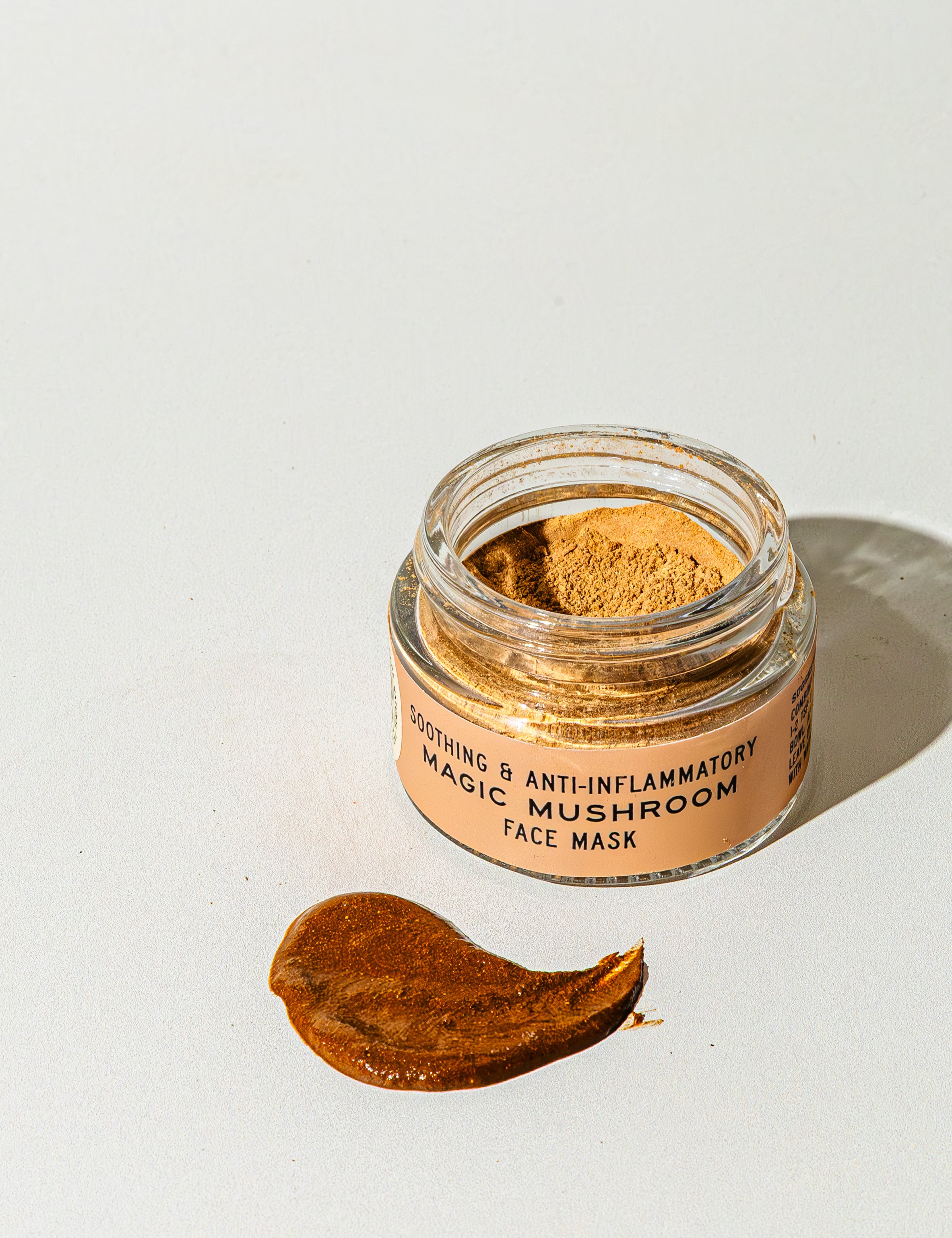 A small open jar labeled TESTER — Magic Mushroom Face Mask from Good Flower Farm sits on a white surface, with a smear of the nourishing mushroom skincare mask spread beside it.