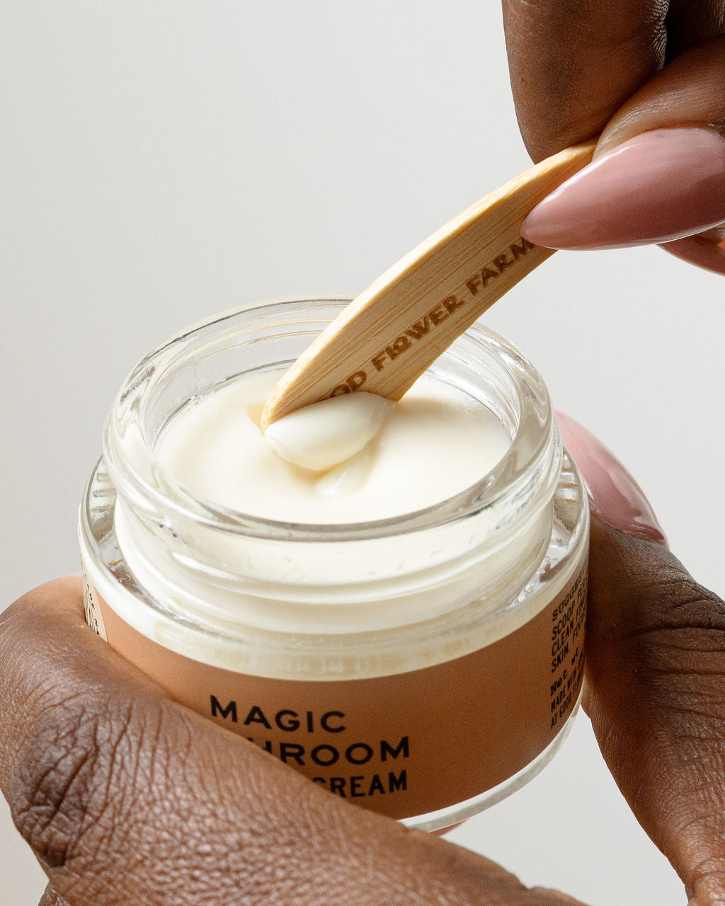 A person uses a Good Flower Farm Reusable Bamboo Spatula to scoop cream from a jar, with neatly manicured nails and the jar held in their other hand.