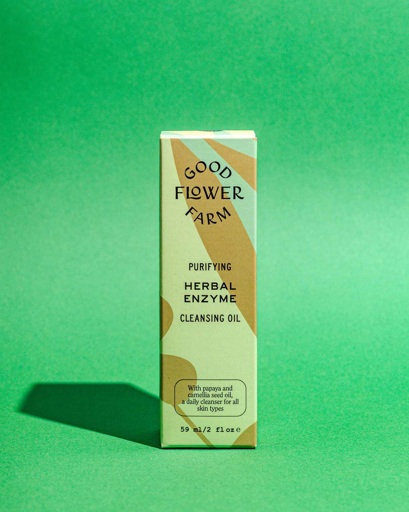 A box of Good Flower Farm Herbal Enzyme Cleansing Oil stands upright on a green background. The earthy packaging highlights this nourishing oil-to-milk cleanser, enriched with papaya seed oil for an effective, purifying cleanse.