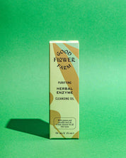 A box of Good Flower Farm Herbal Enzyme Cleansing Oil stands upright on a green background. The earthy packaging highlights this nourishing oil-to-milk cleanser, enriched with papaya seed oil for an effective, purifying cleanse.