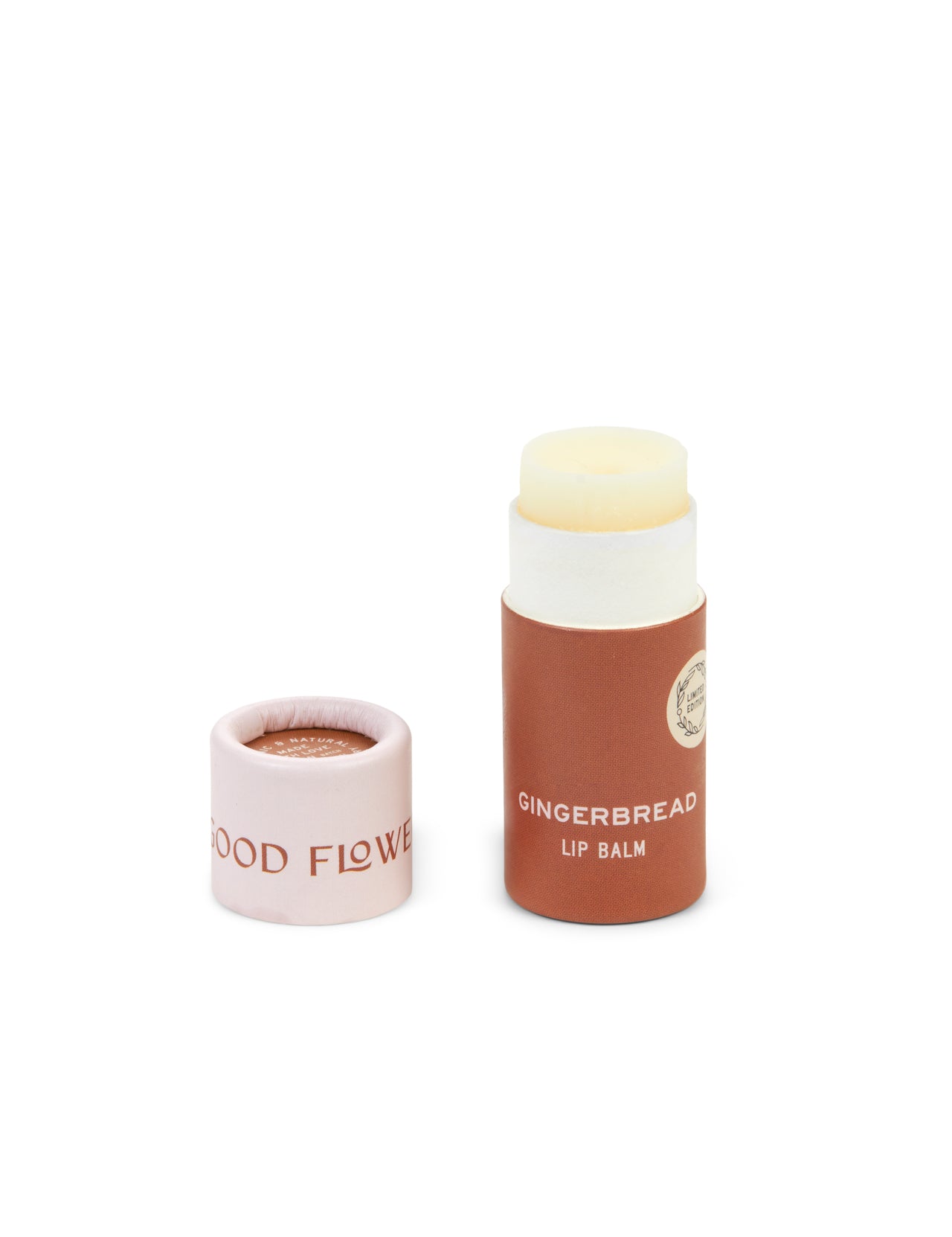 A tube of SEASONAL LIMITED Gingerbread Organic Lip Balm by Good Flower Farm with its light pink GOOD FLOWER cap removed and placed beside it. The brown, biodegradable tube has white text and a round label for an eco-friendly, stylish look.