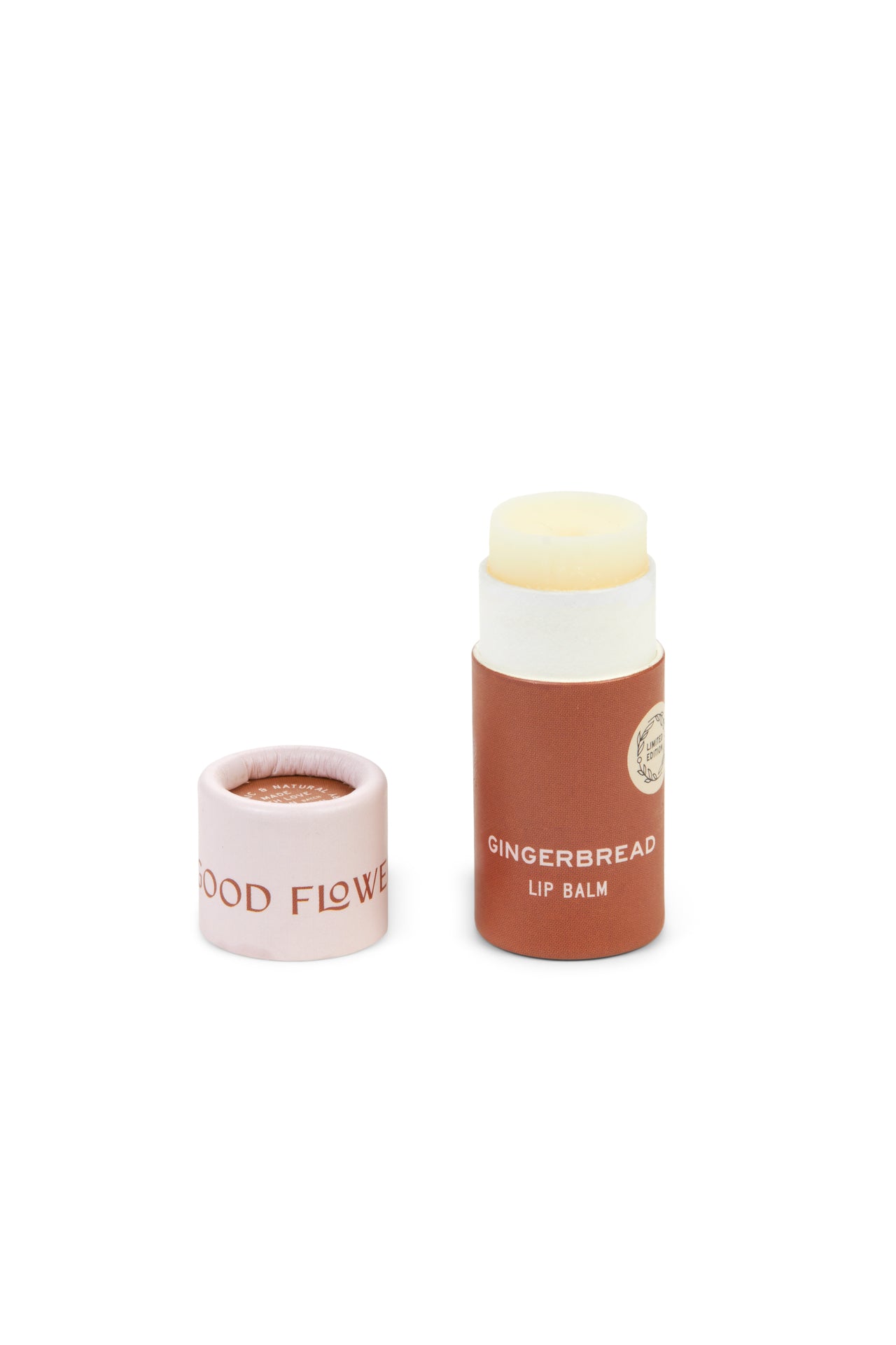 A tube of SEASONAL LIMITED Gingerbread Organic Lip Balm by Good Flower Farm with its light pink GOOD FLOWER cap removed and placed beside it. The brown, biodegradable tube has white text and a round label for an eco-friendly, stylish look.