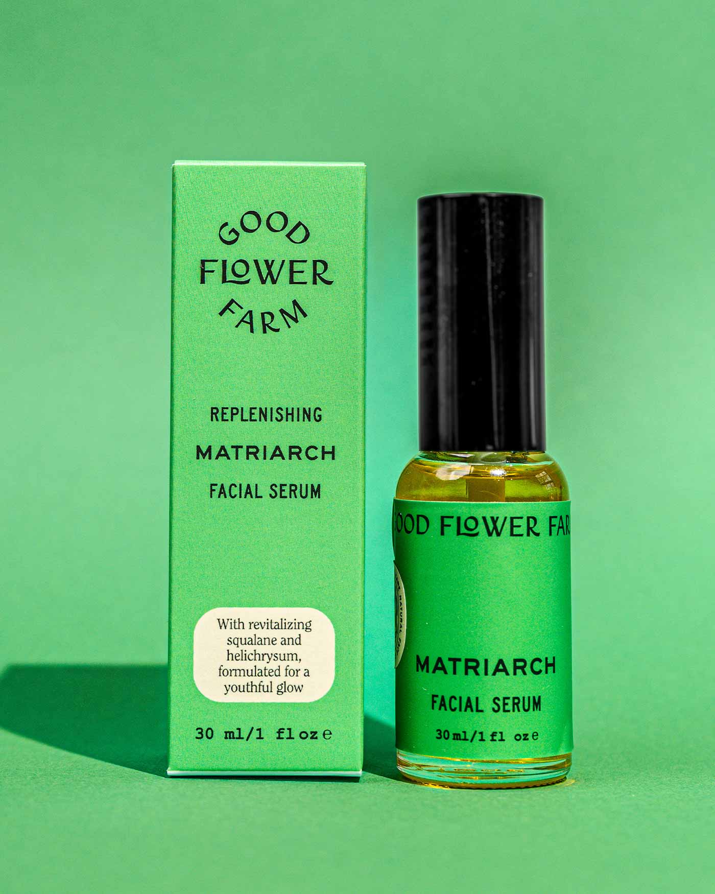 A green bottle of Good Flower Farm’s Matriarch Facial Serum sits beside its box on a green background, with packaging featuring nourishing ingredients such as vitamin E, squalane, and helichrysum for radiant skin.