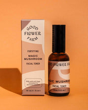 A bottle and box of Good Flower Farm Magic Mushroom Facial Toner on a brown-orange background, featuring reishi and chaga for skin hydration and protection. The packaging displays the 59 ml (2 fl oz) size.