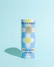 A cylindrical container of TESTER — Good Baby Petal Powder by Good Flower Farm stands upright on a light blue background, adorned with large white and yellow flowers, and features biodegradable, eco-friendly packaging.