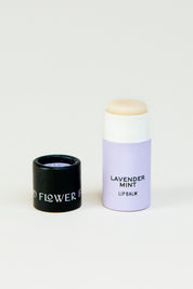 A lavender-colored tube of Seconds Lip Balm by Good Flower Farm stands upright with its black cap, displaying partial text on a white background—showing that even imperfect lip balms can provide beautiful inside lip care.