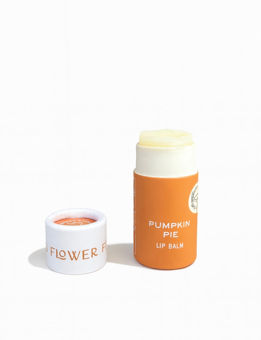 A tube of Good Flower Farm’s SEASONAL LIMITED Pumpkin Pie Organic Lip Balm, cap off and beside it. The orange and white tube contains pale yellow balm made with coconut oil for soft, smooth lips.