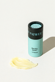 A tube of Basil Mint Lip Organic Lip Balm with a teal label and a smear of moisturizing yellow balm in front.