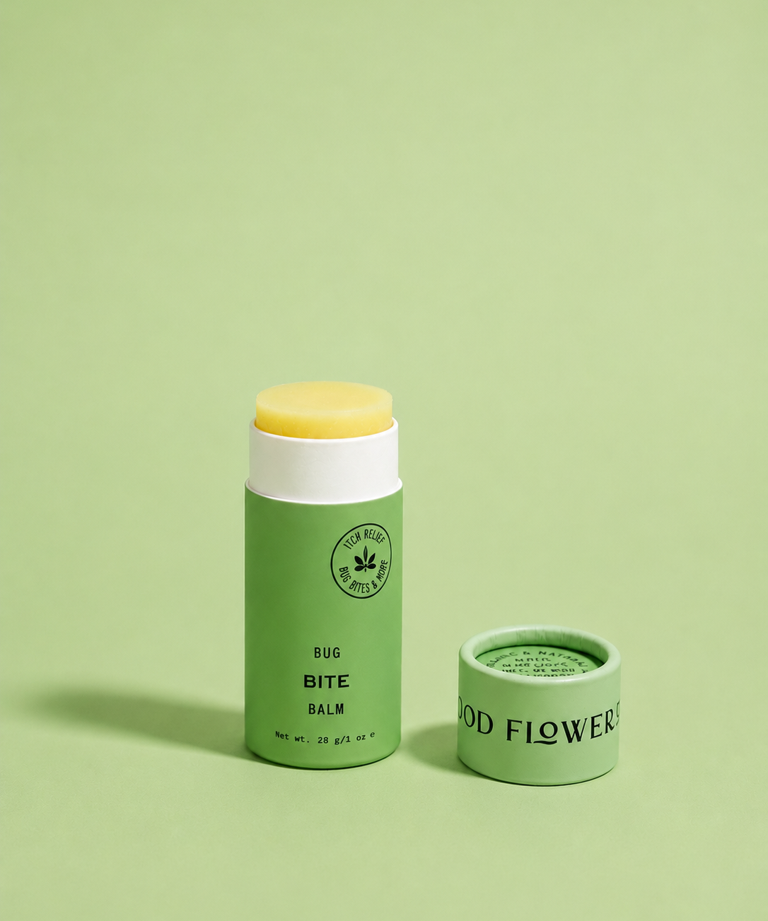 A green tube of Good Flower Farm Bug Bite Balm For Anti-Itch stands upright with its lid off on a matching green background, revealing the yellow balm inside. The lid is placed beside the tube.