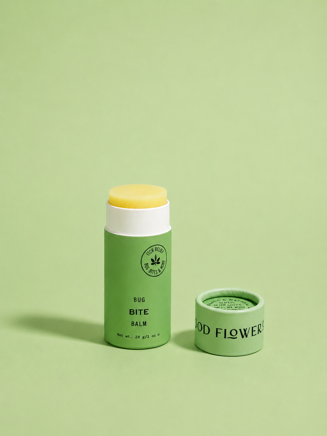 A green tube from the good-flower-farm Seasonal Skincare Bundle sits with its cap off, revealing the yellow balm inside, all arranged on a light green background.
