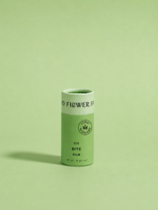 A cylindrical container from good-flower-farm’s Seasonal Skincare Bundle stands upright on a green background, featuring a green label with a circular emblem and branding.