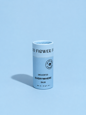 A cylindrical tube of Good Flower Farm’s Everywhere Balm stands upright on a light blue background with a soft shadow to the left. Its light blue packaging features black text.