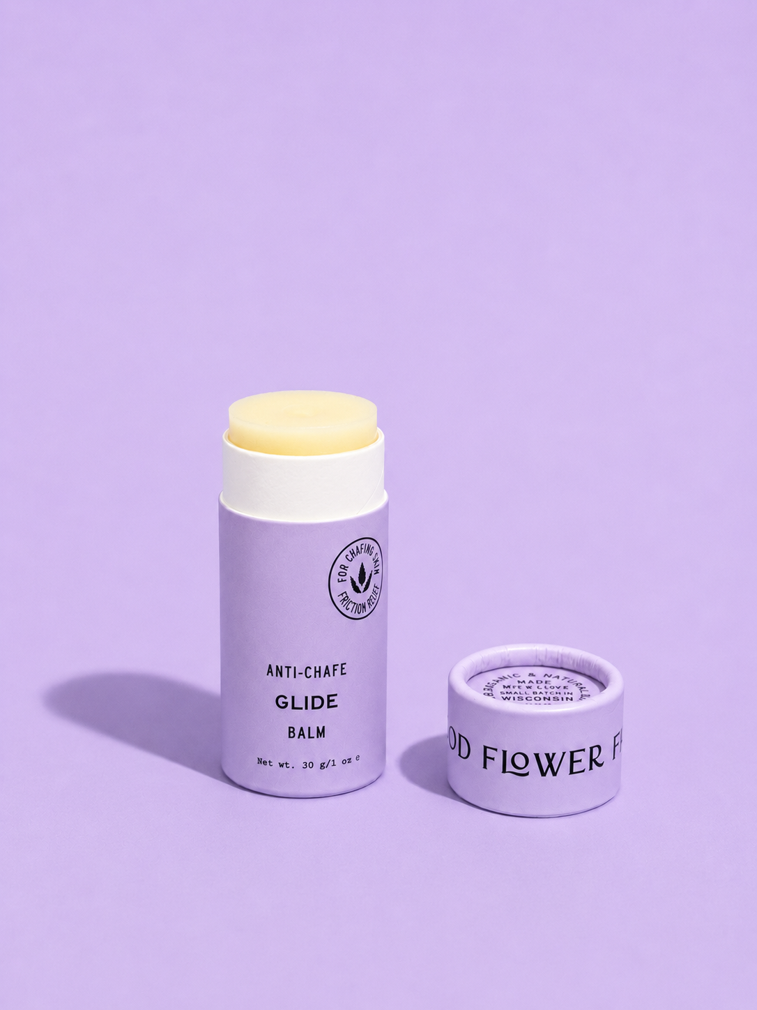 A lavender tube of Good Flower Farm Glide Balm For Anti-Chafe, lid off to reveal the balm, sits on a matching purple surface with its shadow visible.
