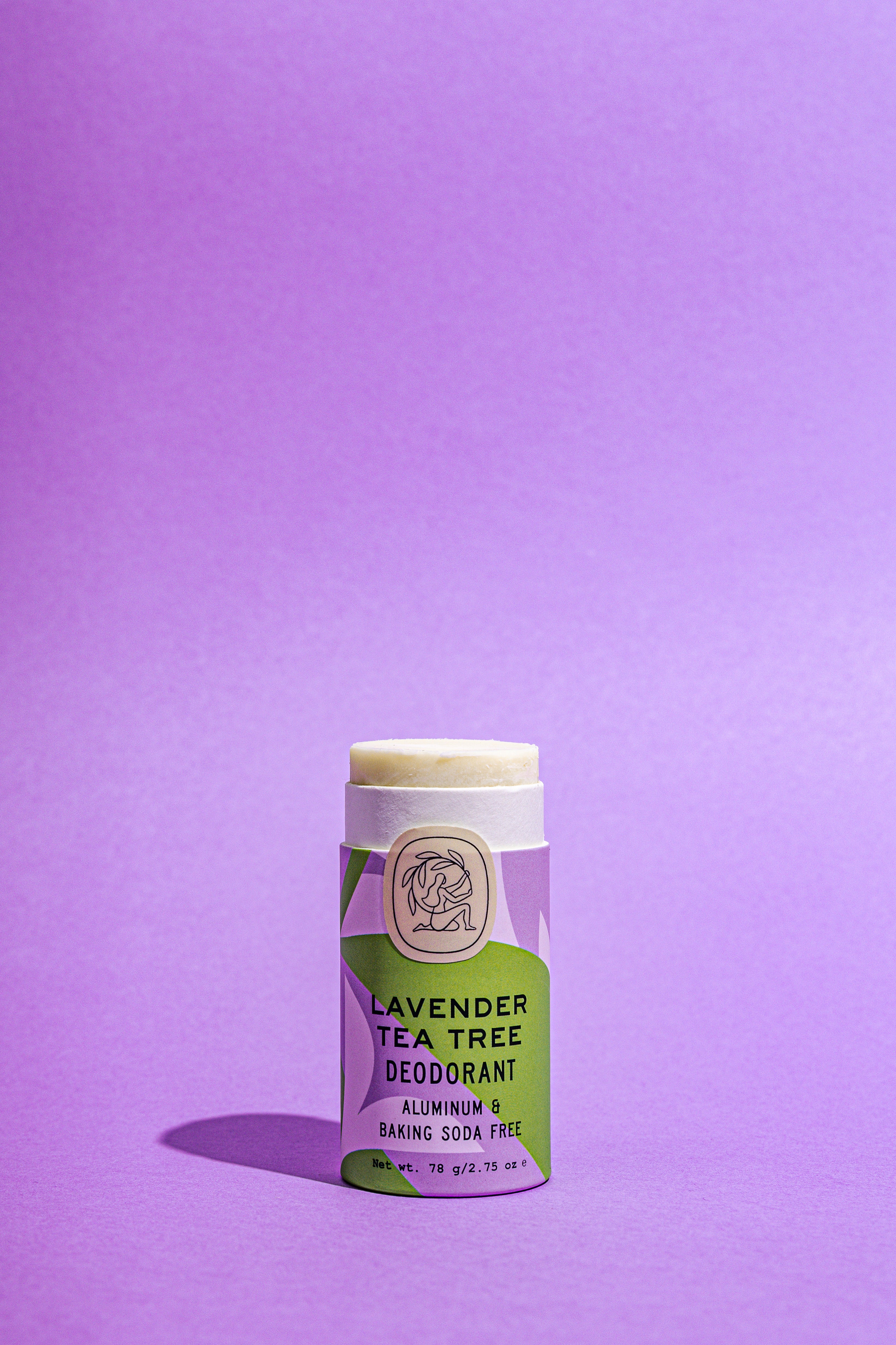 A Good Flower Farm Lavender Tea Tree Deodorant Plastic-Free Tube with a purple and green label stands upright on a purple background. The label notes its aluminum-free, baking soda free, and packaged in biodegradable tubes.