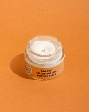 A small glass jar from good-flower-farm’s Dry Skin Bundle: Save 15% rests on an orange surface, filled with a creamy white moisturizer—ideal for facial hydration and soothing dry skin.
