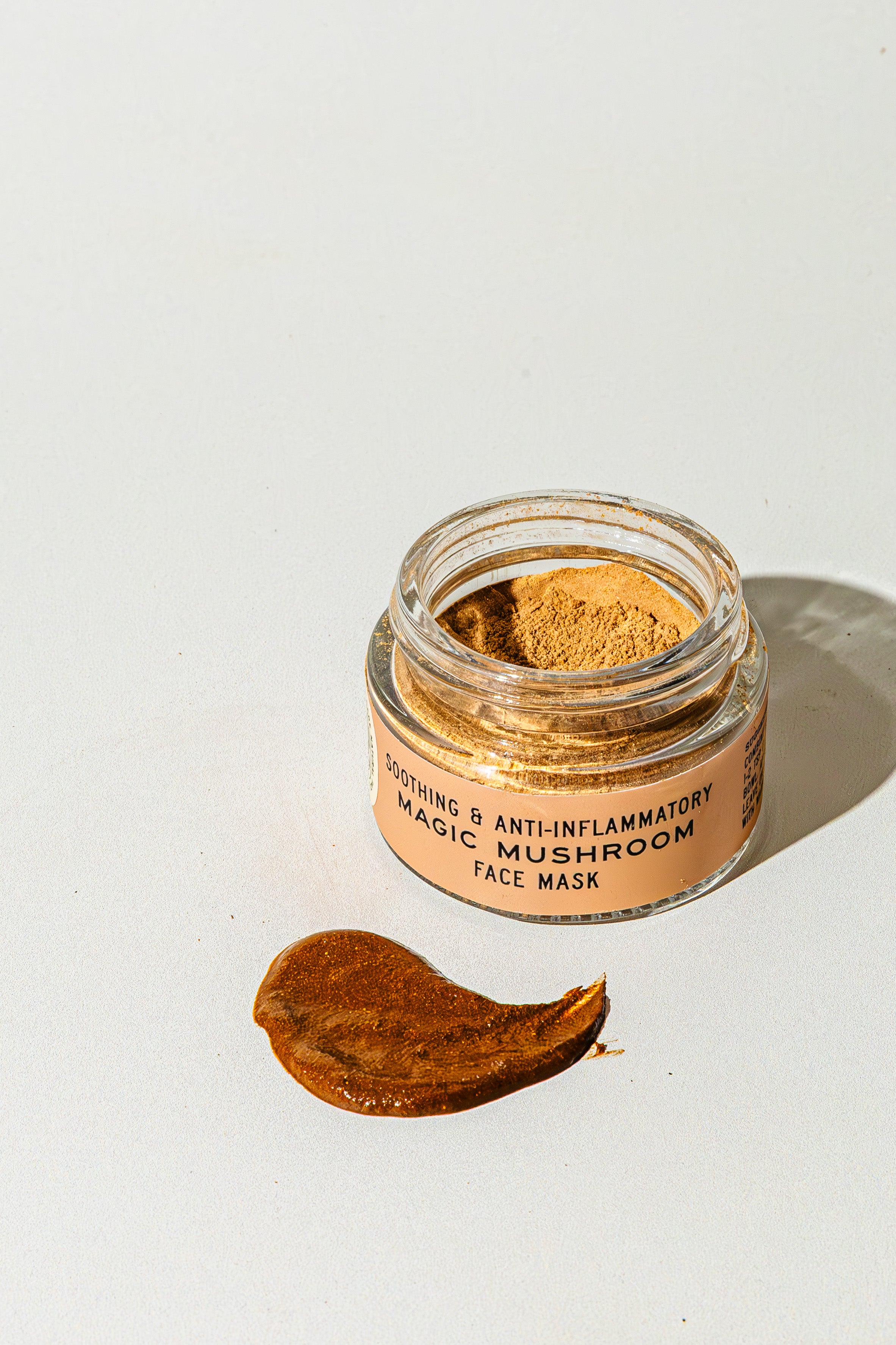 A small open jar labeled TESTER — Magic Mushroom Face Mask from Good Flower Farm sits on a white surface, with a smear of the nourishing mushroom skincare mask spread beside it.