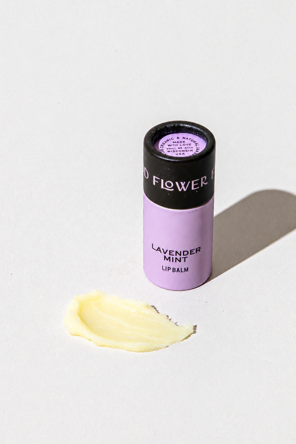 Lavender Mint Organic Lip Balm in a purple cylindrical tube, accompanied by a small smear of the eco-friendly product beside it.