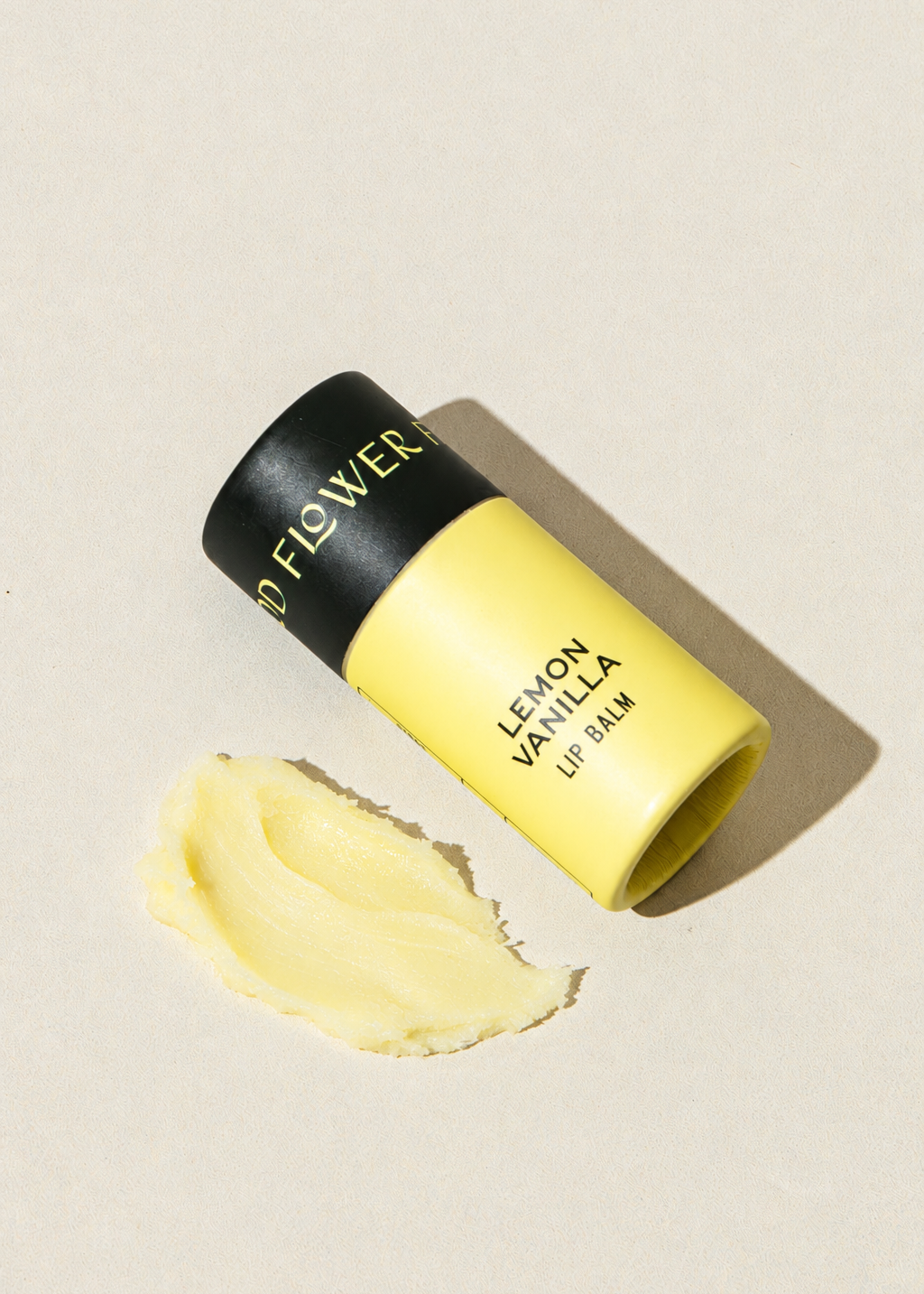 Yellow cardboard tube of Good Flower Farm Lemon Vanilla Organic Lip Balm with a smear of product next to it.