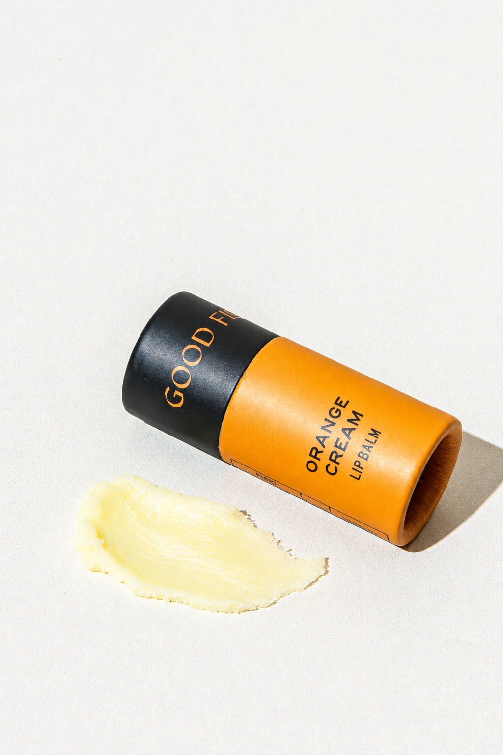 An eco-friendly Orange Cream Organic Lip Balm tube with an orange label next to a smear of yellow coconut oil balm.