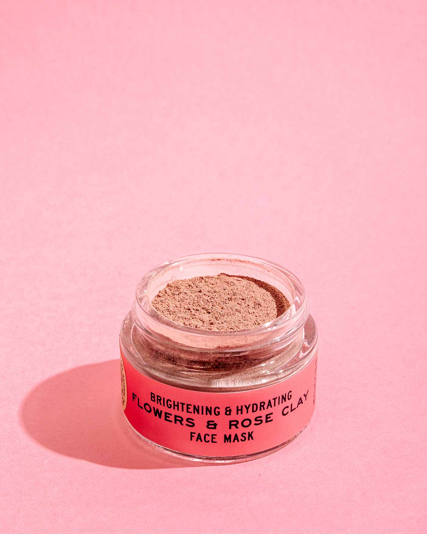 A small open jar from the good-flower-farm Dry Skin Bundle: Save 15% sits on a pink surface, the label visible and powdery product inside exposed—an ideal companion to moisture cream for dry skin and facial moisturizing.