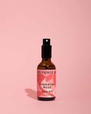 A brown spray bottle from good-flower-farm’s Seasonal Skincare Bundle stands on a pink surface with a pink background, casting a soft shadow to the left.