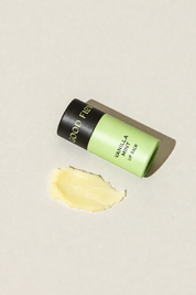 A small tube of Good Flower Farm Vanilla Mint Organic Lip Balm with shea butter and a smear of yellow balm next to it.