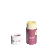A tube of Good Flower Farm SEASONAL LIMITED Sugar Plum Organic Lip Balm stands upright with its cap off and beside it, revealing the moisturizing, eco-friendly balm inside. The lip balm features a purple Sugar Plum label and is set against a plain white background.